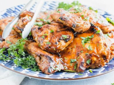 juicy grilled chicken thighs on a plate with tongs off to the side