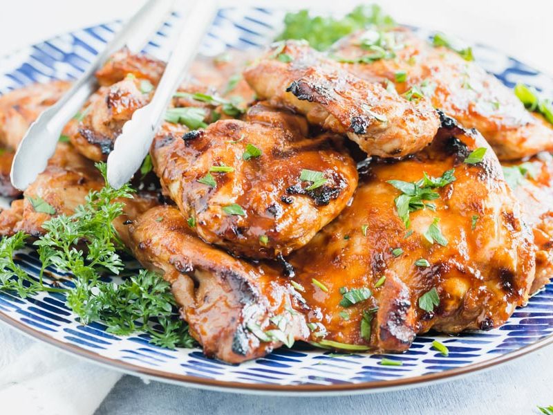 juicy grilled chicken thighs on a plate with tongs off to the side