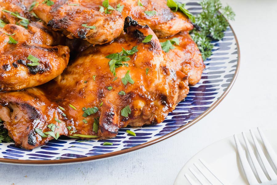 juicy bbq chicken on a serving plate next to forks and parsley