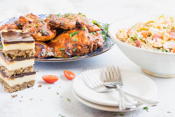 a summertime dinner spread of huli chicken, salad and dessert with two plates and some forks