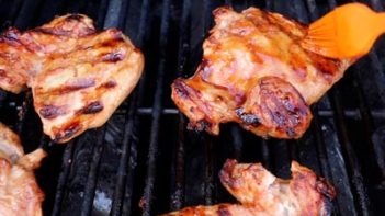 basting chicken on a grill with a marinade and a brush
