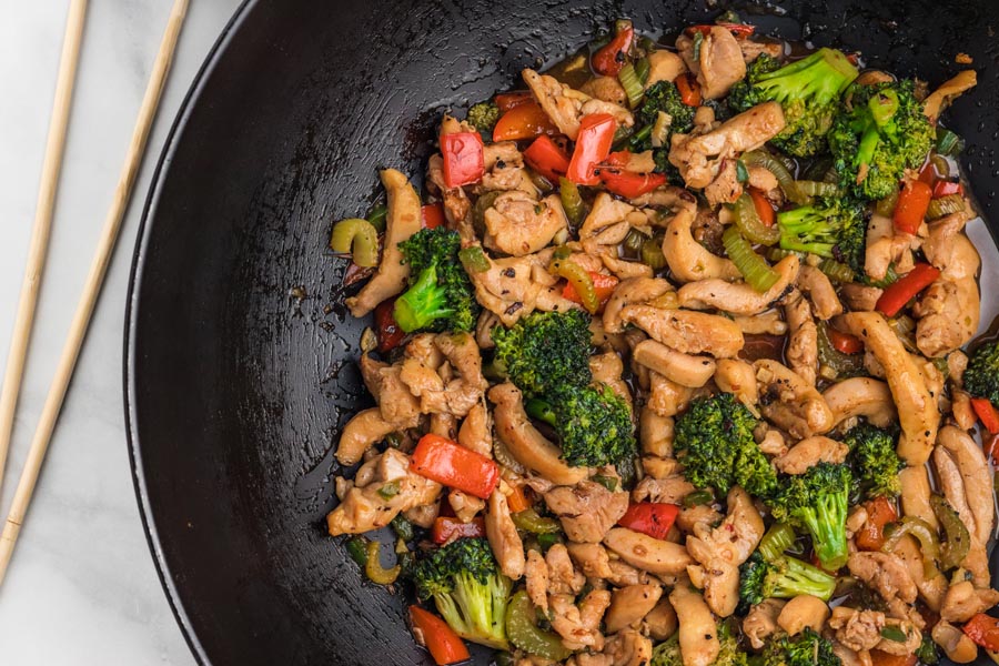 Stir fry chicken in a wok with broccoli and red peppers.