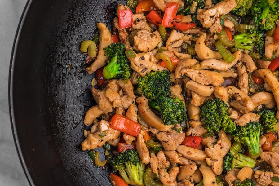 Close up of hunan chicken stir fry in a wok with colorful vegetables like broccoli, celery and red peppers.