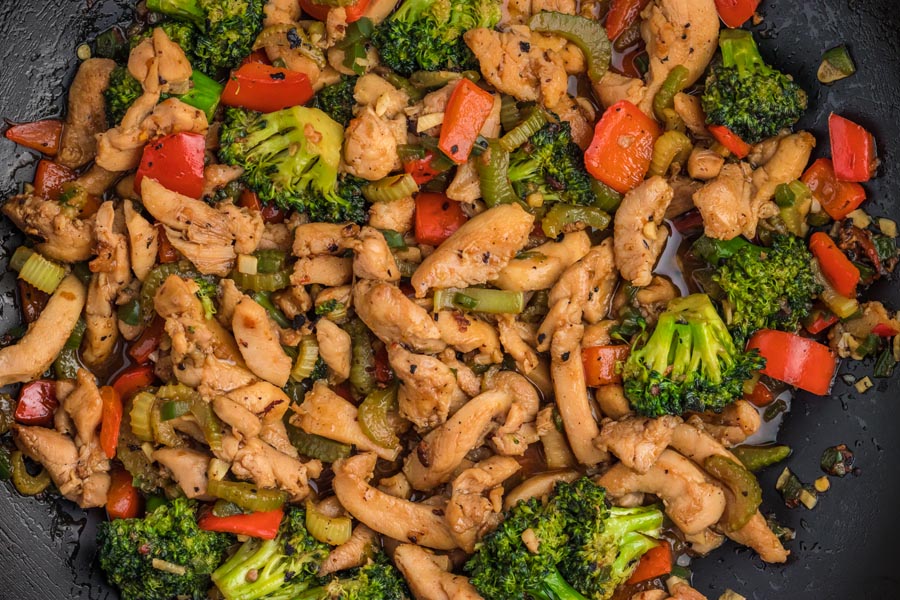 Stir fry of sliced chicken, broccoli and chunks of red pepper in a black wok.