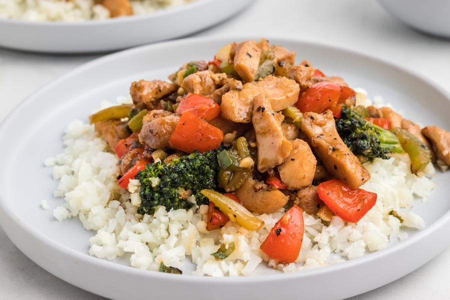 Colorful hunan chicken stir fry over a bed of cauliflower rice on a plate.