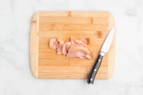 A wooden cutting board with sliced chicken thighs and a knife on top.