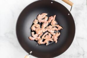 A wok with sliced chicken pieces cooking.