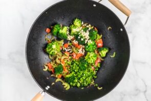 A wok with broccoli, peppers and other vegetables cooking.