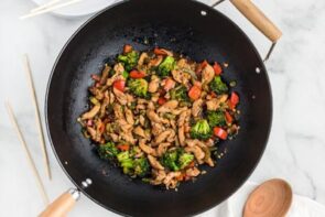 A finished stir fry mixture of hunan chicken with vegetables next to chopsticks.