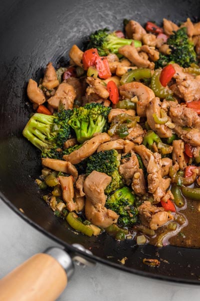 A wok with chicken stir fry mixed with broccoli and red bell peppers.