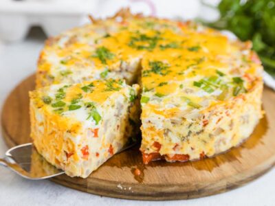 Instant Pot breakfast casserole with sausage, eggs, cheese, peppers, onions, and green onions sliced on a wooden serving board.