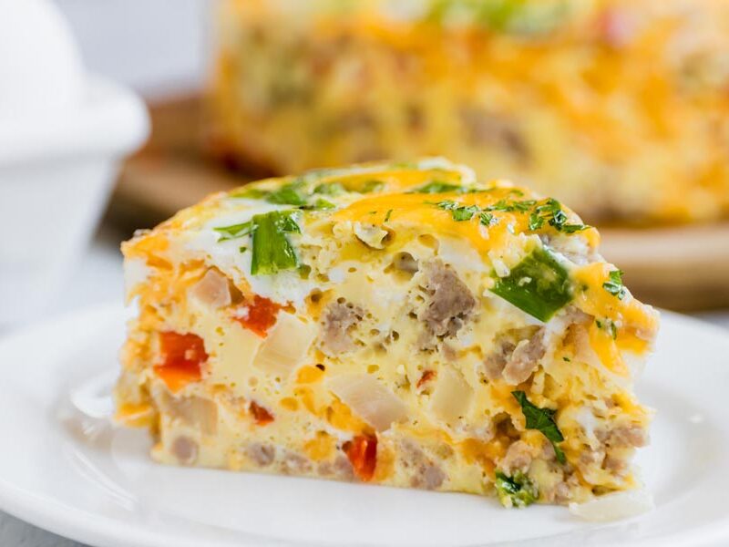 Thick slice of Instant Pot breakfast casserole showing fluffy eggs, breakfast sausage, vegetables, and melted cheddar cheese.