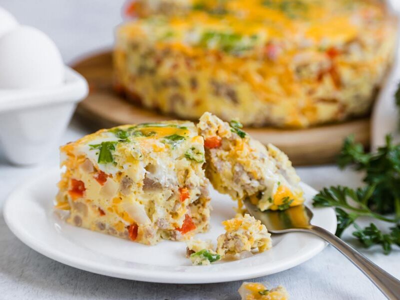 Slice of Instant Pot breakfast casserole with sausage, cheese, peppers, and onions being cut with a fork.
