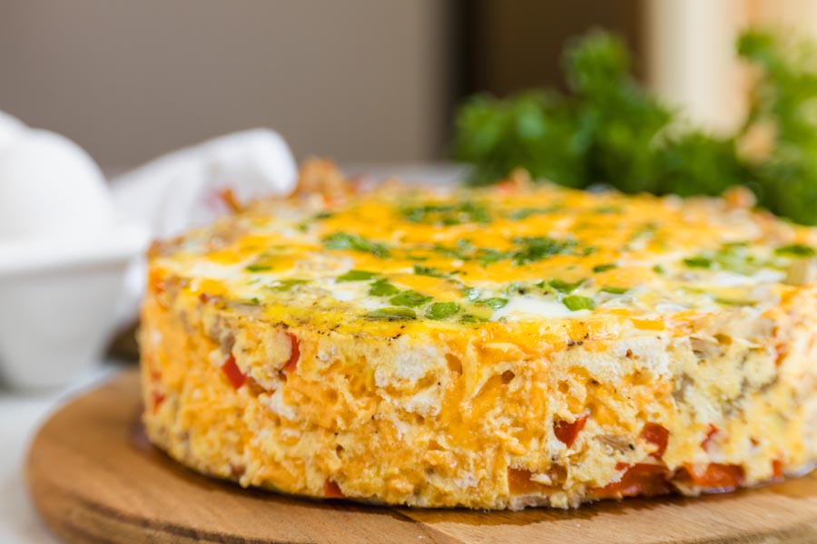 Close-up of a whole Instant Pot breakfast casserole with sausage, vegetables, cheddar cheese, and fresh herbs.