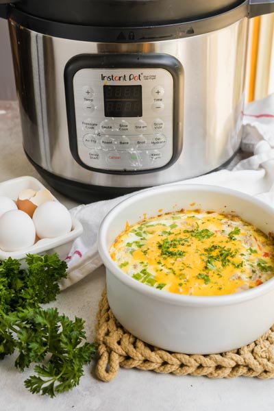 Instant Pot breakfast casserole in a round baking dish served beside eggs and fresh parsley.