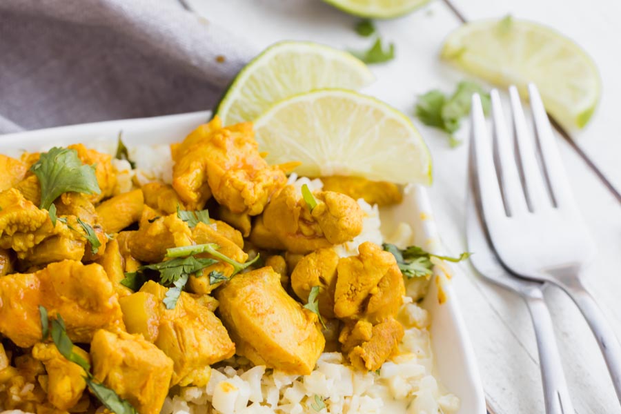 close up of buttery chicken on a bed of cauliflower rice with lime slices