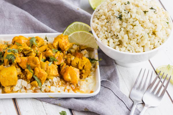 a plate with orange butter chicken next to a big bowl of rice