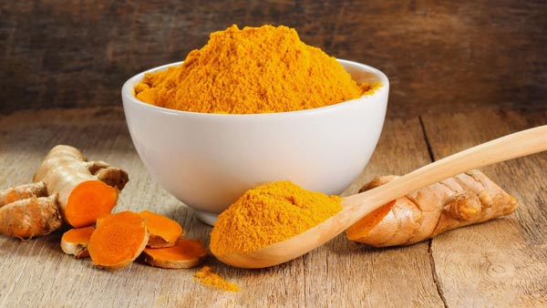 a bowl of orange powdered turmeric next to a root