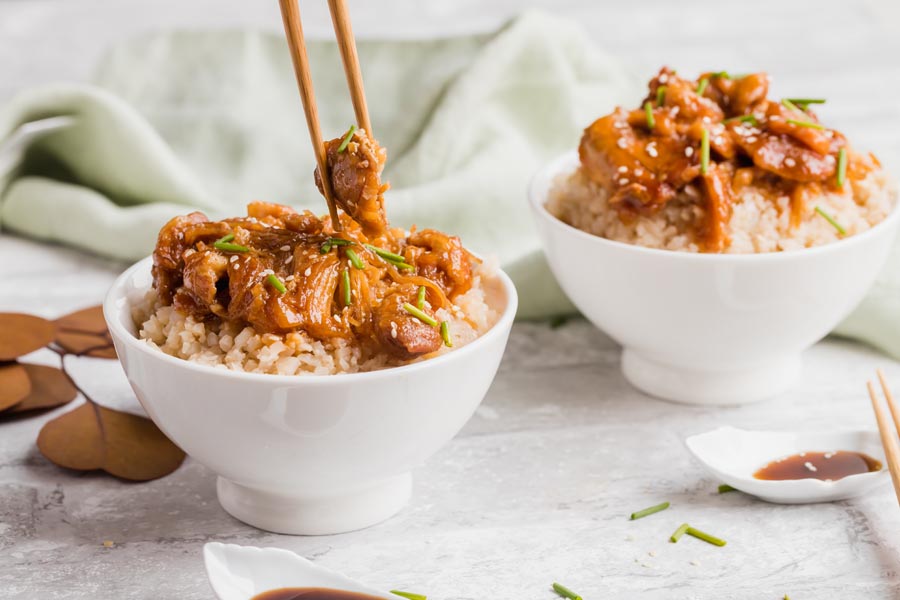 picking up sesame chicken with chopsticks from a white bowl