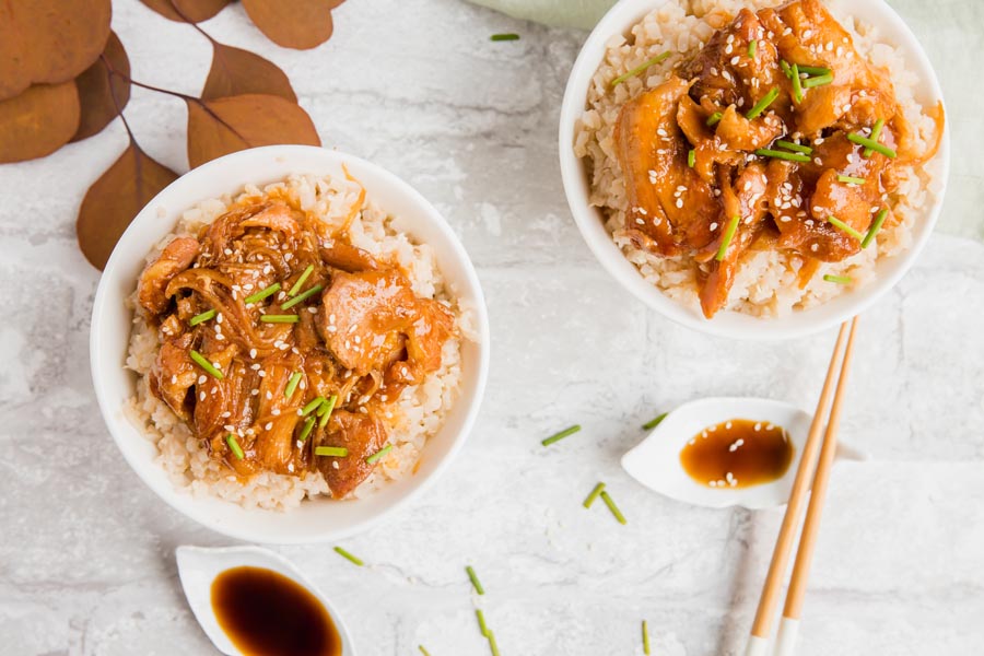 looking down into two dinner bowls with sesame chicken over keto rice