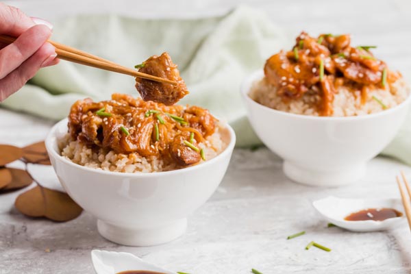 holding a piece of sesame chicken with chopsticks