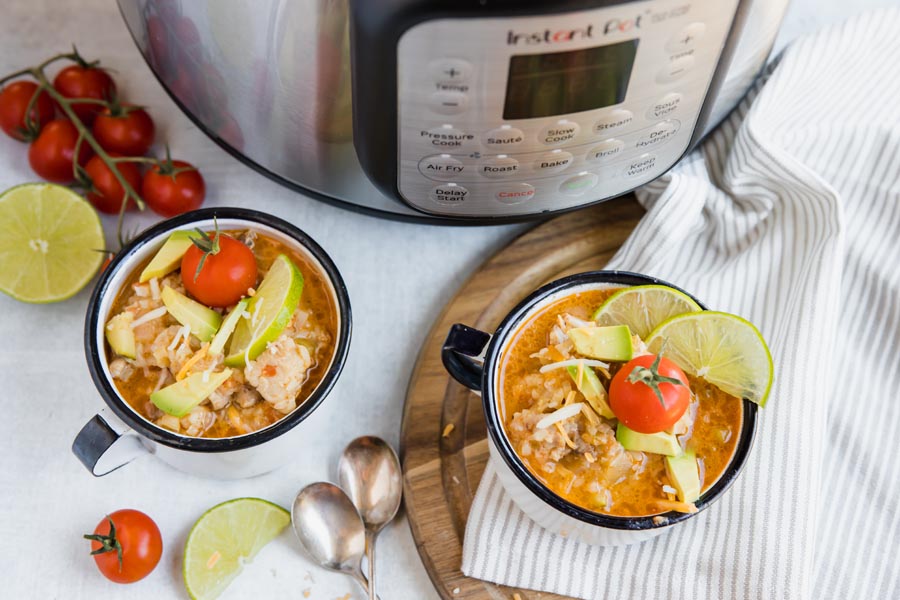 an instant pot sits next to two rice bowls with tomatos and limes scattered around