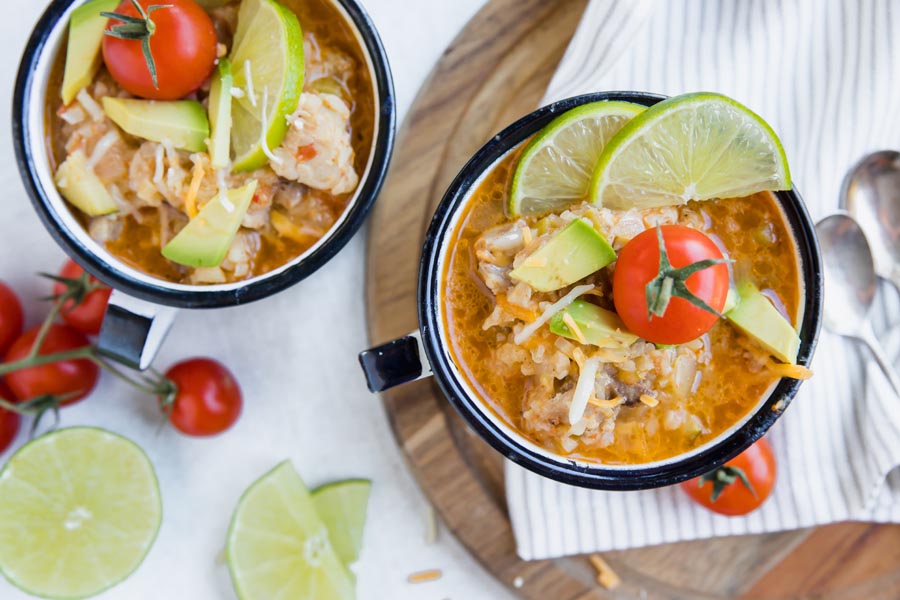 overhead view of two cups with chicken and rice dish in them topped with lime wedges and tomatos