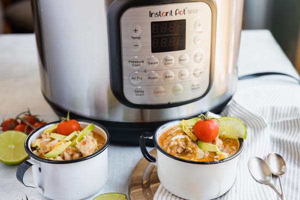 two bowls of chicken and rice topped with cheese and tomatoes are sitting next to an instant pot pressure cooker on the counter