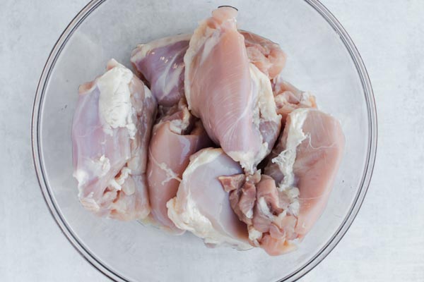 a bunch of raw chicken thighs in a clear bowl on the counter