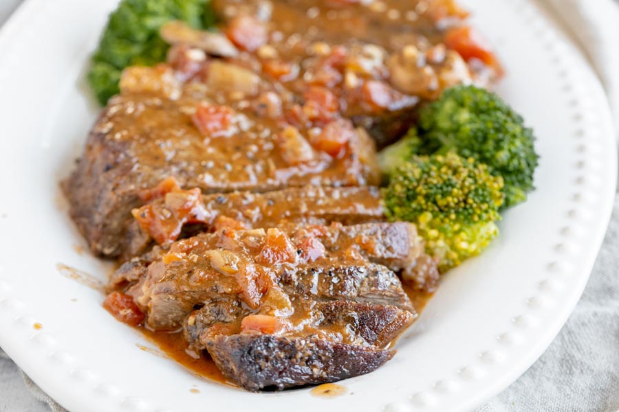 juicy steak sliced on a platter and covered in a tomato based sauce with broccoli florets on the platter too
