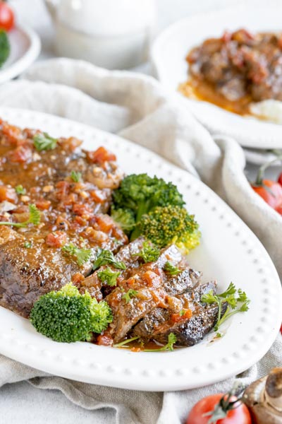 a dinner platter with sliced steak and broccoli topped with a tomato sauce