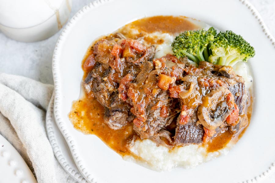 steak topped with tomatoes and mushrooms over mashed potatoes and a side of cauliflower