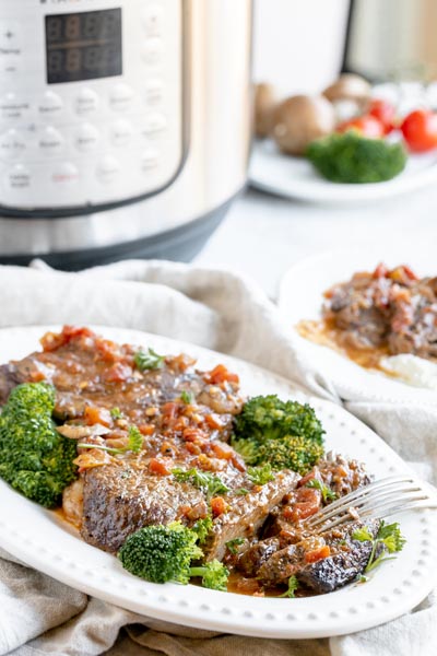 juicy steak on a platter with broccoli and mushrooms around with an instant pot in the background