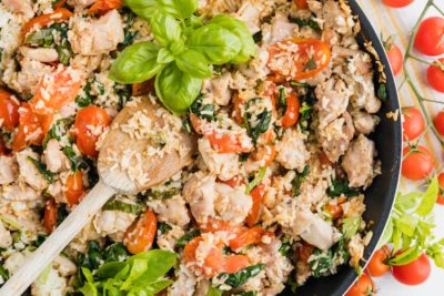 a large skillet with fresh tomatoes, spinach and chicken topped with basil