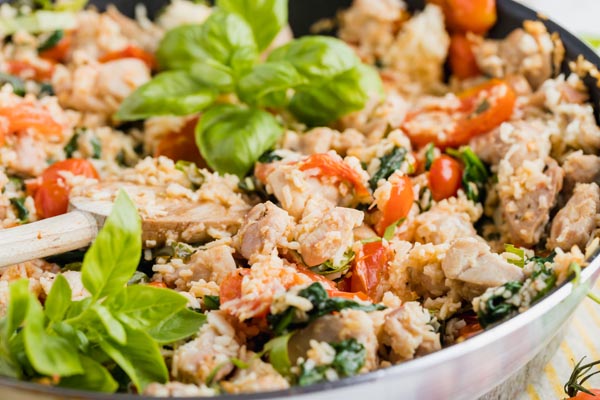 chicken with tomatoes and spinach with keto rice in a skillet topped with fresh basil