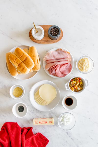 Ingredients for Italian sandwiches on keto hot dog buns including provolone, ham and salami.