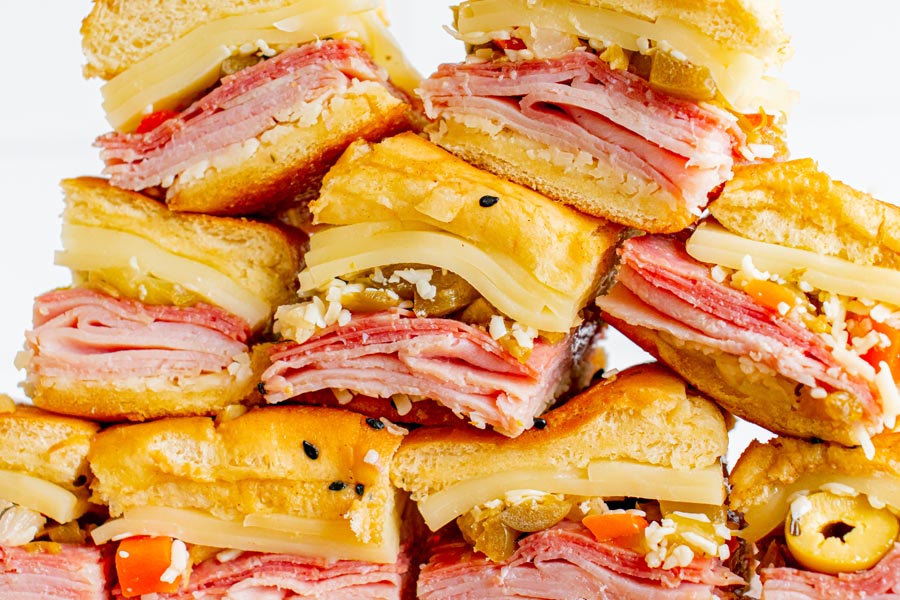 A stack of mini sub sandwiches filled with italian meats and cheese and muffuletta olive spread.