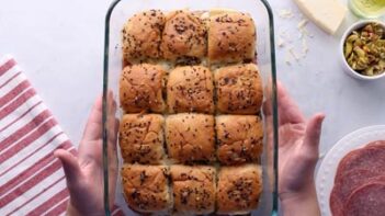 Hands holding a casserole dish filled with baked sliders.