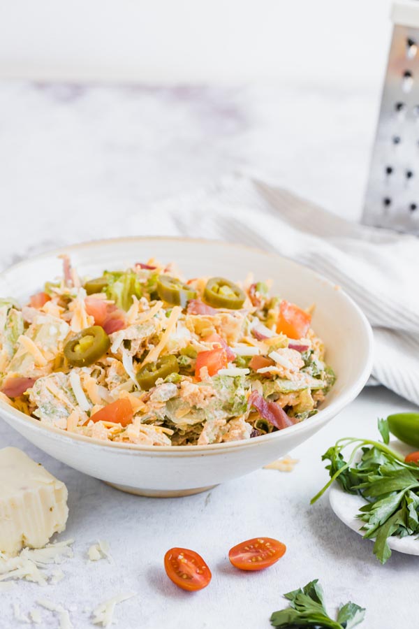 a bowl of keto salad next to tomatoes, parsley and cheese