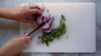 chopping up red onion with a knife while diced jalapeno is to the side