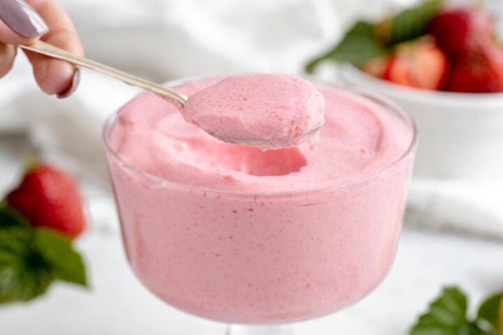 holding a spoonful of fluffy jello dessert over a bowl of pink creamy pudding