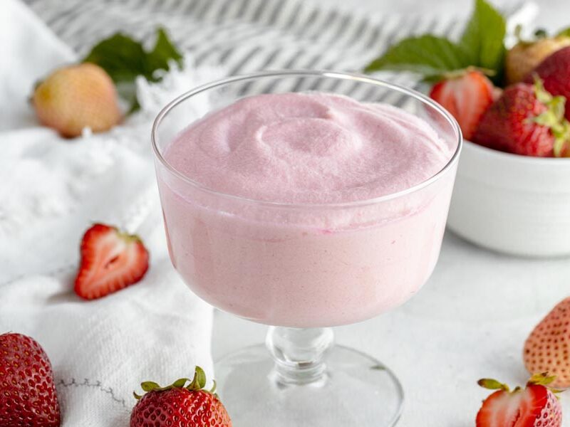 a bowl of pink jello desert surrounded by strawberries