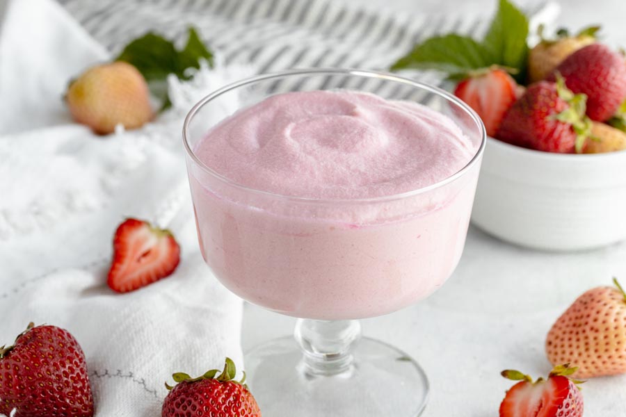 a bowl of pink jello desert surrounded by strawberries