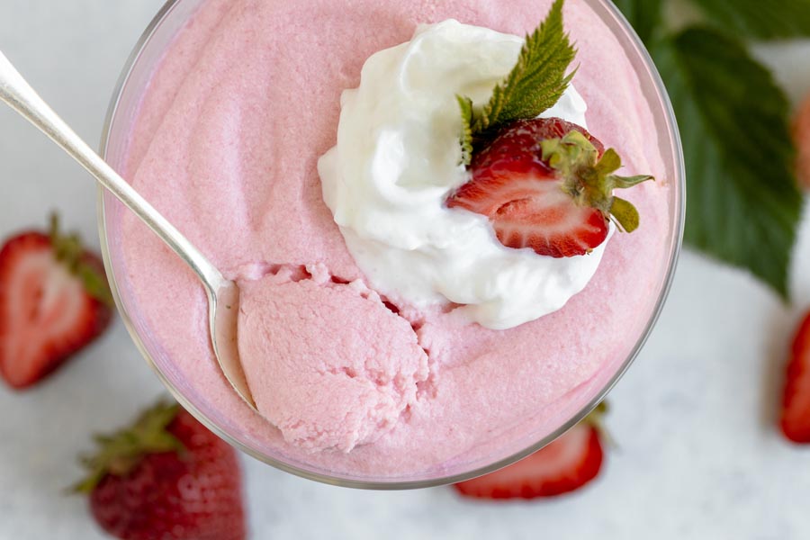 a spoon digging into a pink strawberry jello whip topped with whipped cream and a strawberry