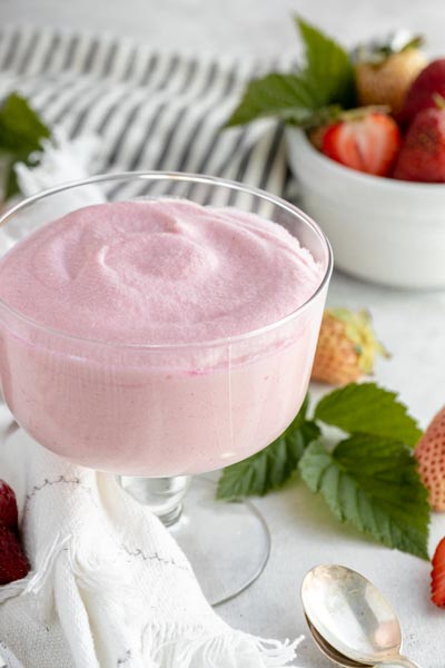 creamy bowl of jello gelatin whip sits by a striped towel and a bowl of strawberries