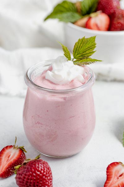 a mason jar with pink jello whip inside topped with whipped cream and a green leaf