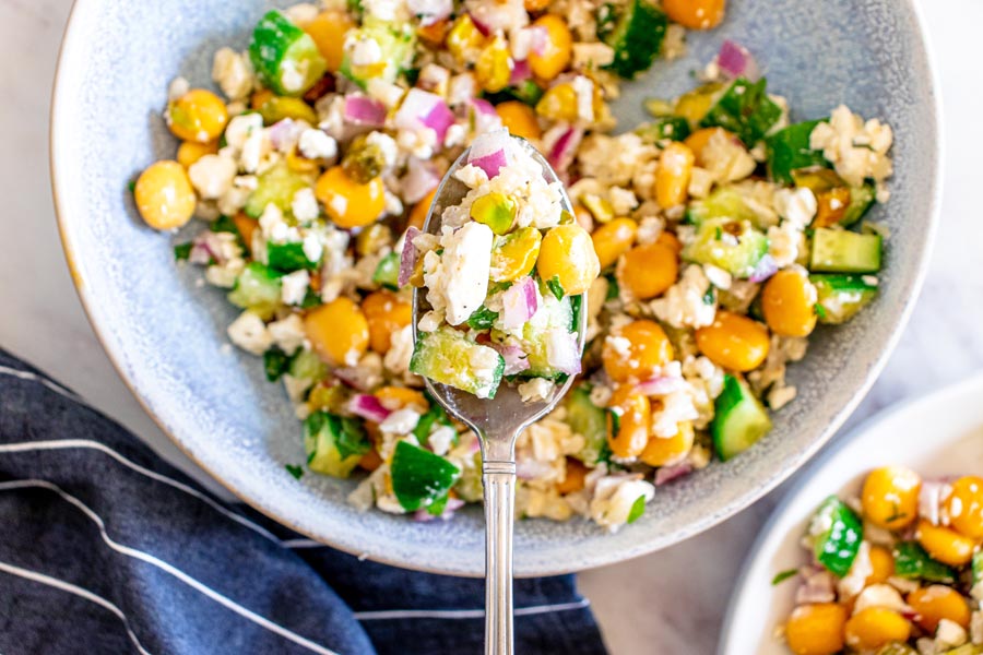 A spoon holding a bite of cauliflower rice salad filled with lupin beans, feta and pistachios over a bowl of more salad.
