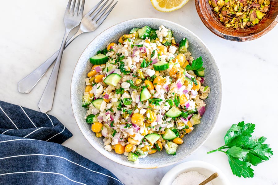 A protein packed salad of lupin beans, pistachios, feta cheese, mint and red onion in a speckled blue bowl with fork and more crushed pistachios near by.