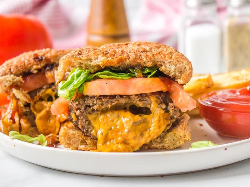 Gooey cheddar cheese oozing out of a hamburger on a plate with ketchup nearby.