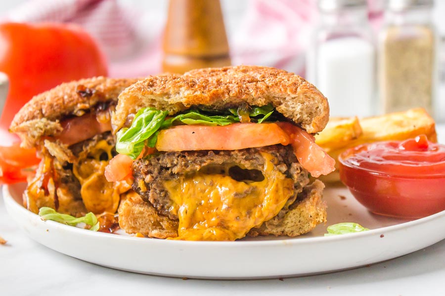 Gooey cheddar cheese oozing out of a hamburger on a plate with ketchup nearby.